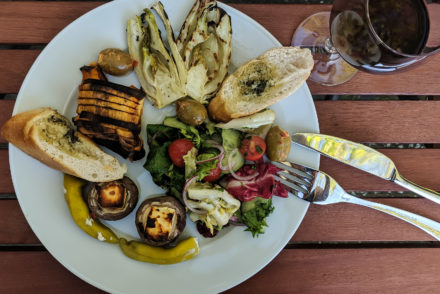 Vegetarisches Barbecue, Teller und Weinglas mit Fenchel, Champignons, Oliven und Kräuterbaguette.
