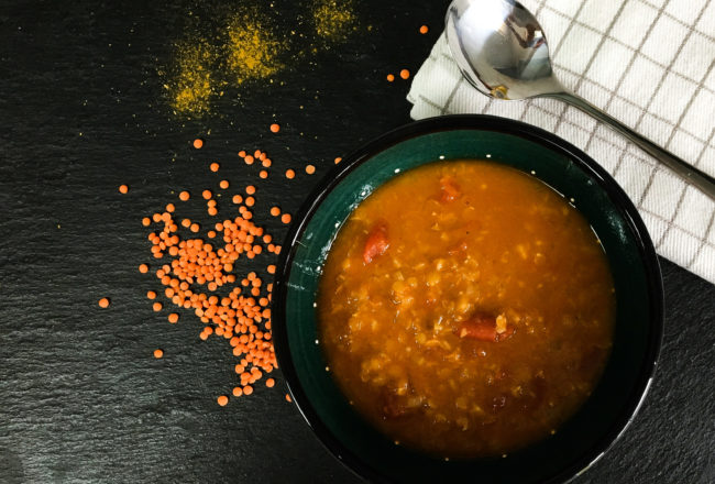 Suppenteller mit Linsen, Currypulver, Küchenhandtuch und Suppenlöffel